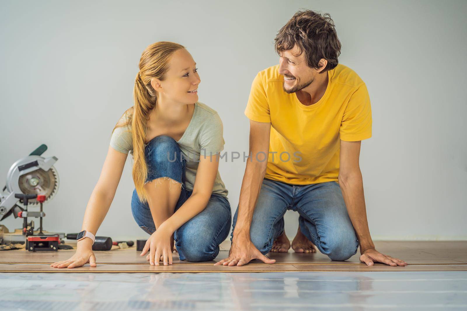 Married couple installing new wooden laminate flooring on a warm film floor. Infrared floor heating system under laminate floor by galitskaya
