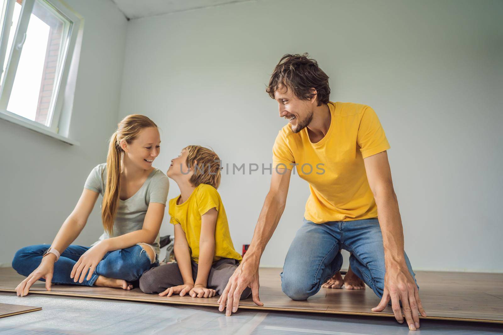 Happy family installing new wooden laminate flooring on a warm film floor. Infrared floor heating system under laminate floor.