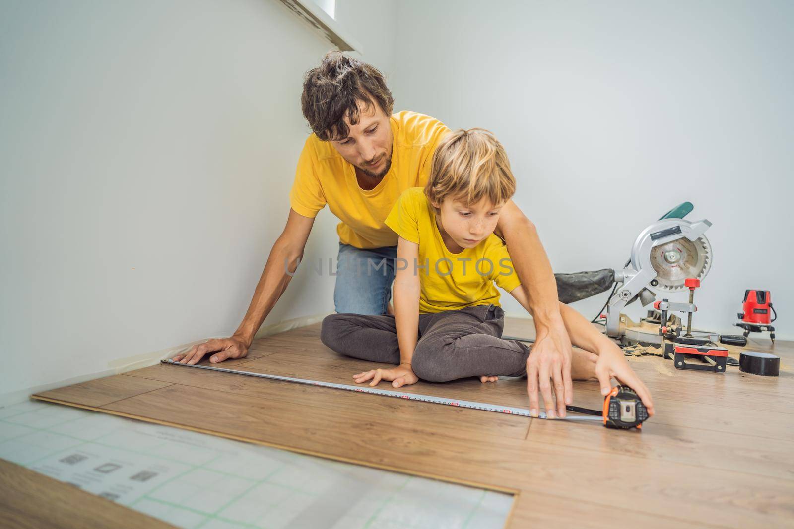 Father and son installing new wooden laminate flooring on a warm film floor. Infrared floor heating system under laminate floor.