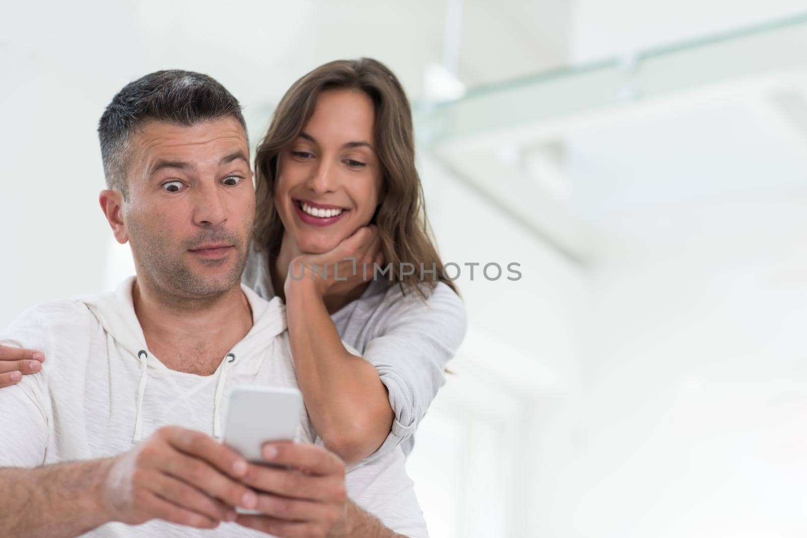 Young happy couple using mobile phone at home together, looking at screen, smiling.