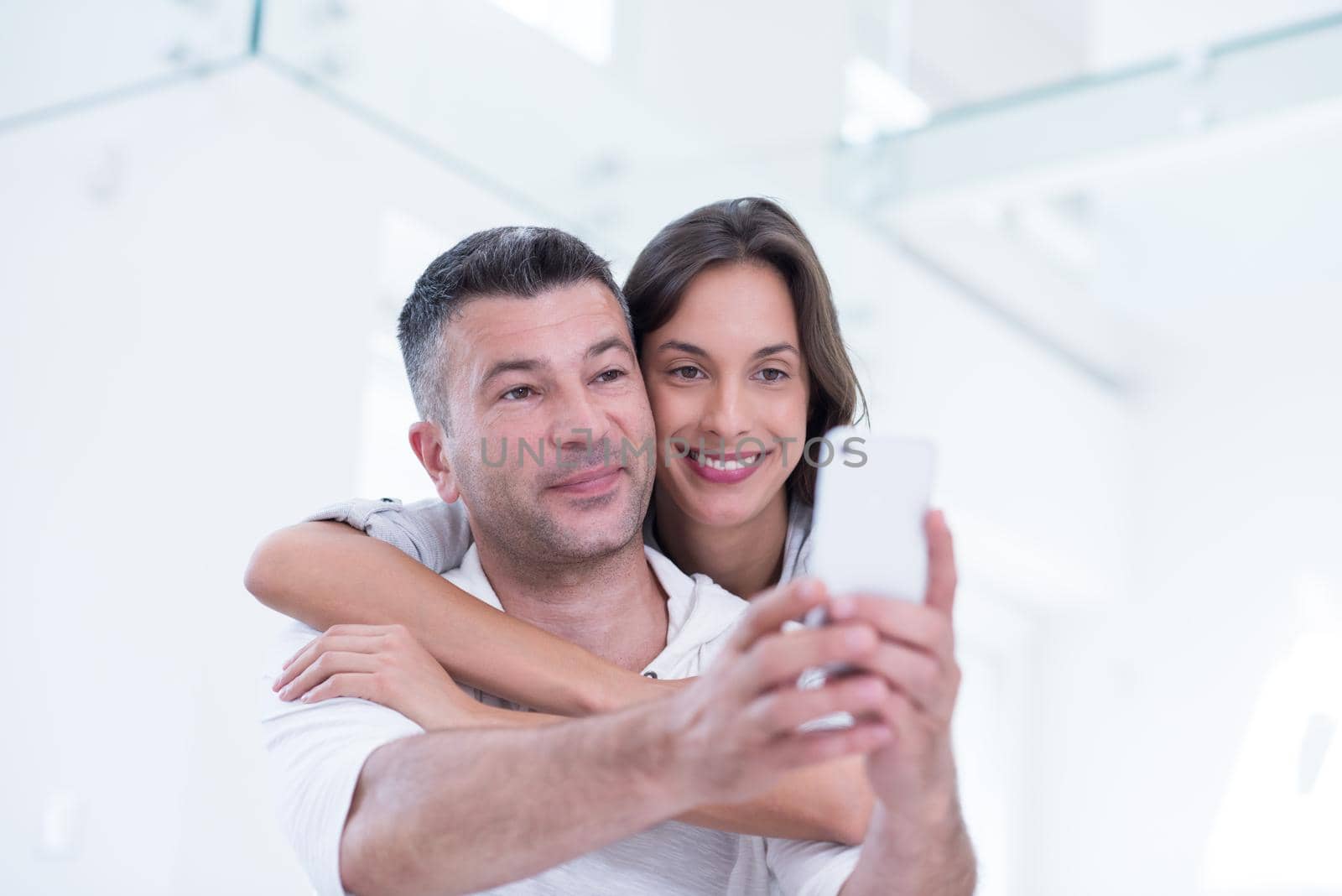 Young happy couple using mobile phone at home together, looking at screen, smiling.