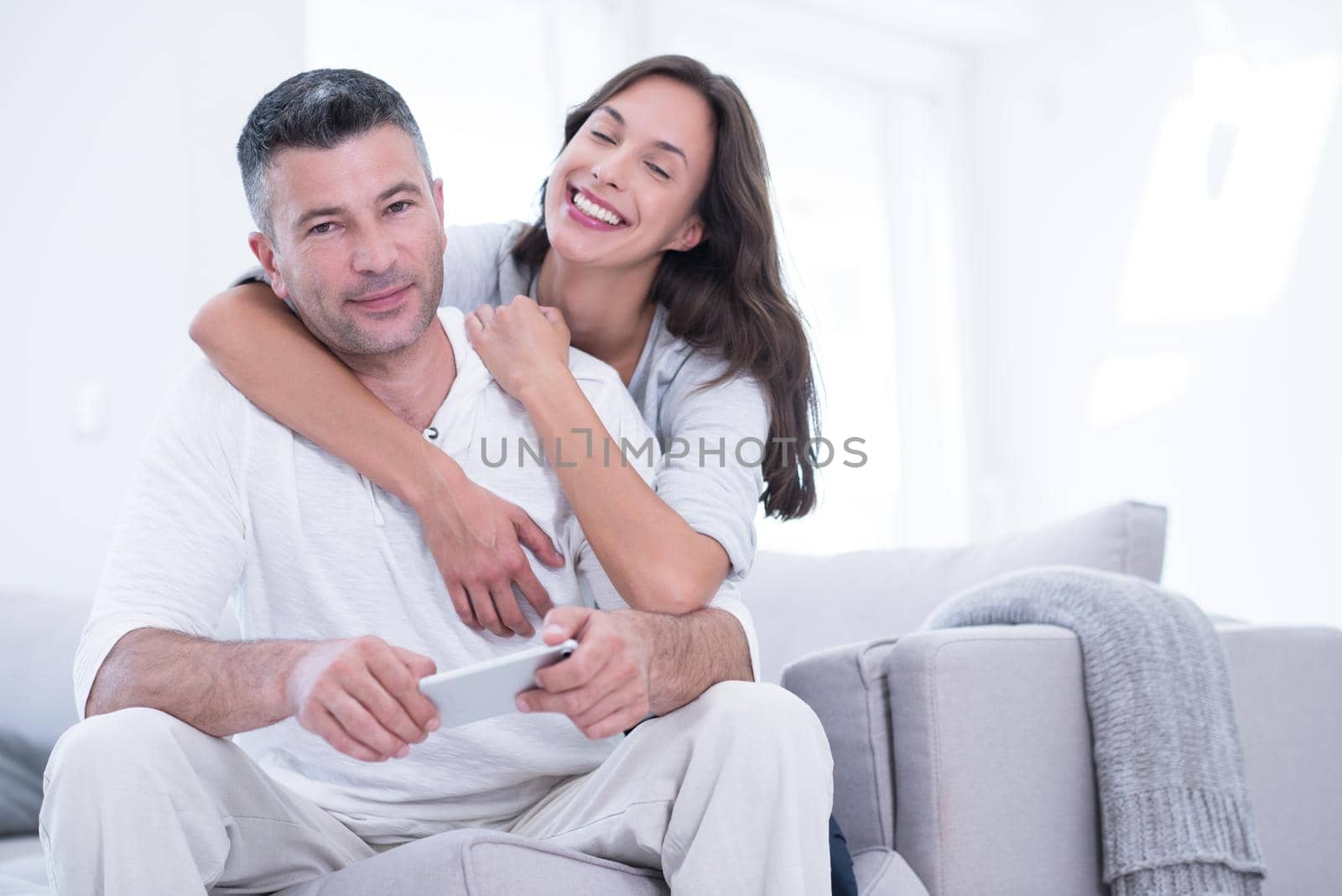 Young happy couple using mobile phone at home together, looking at screen, smiling.