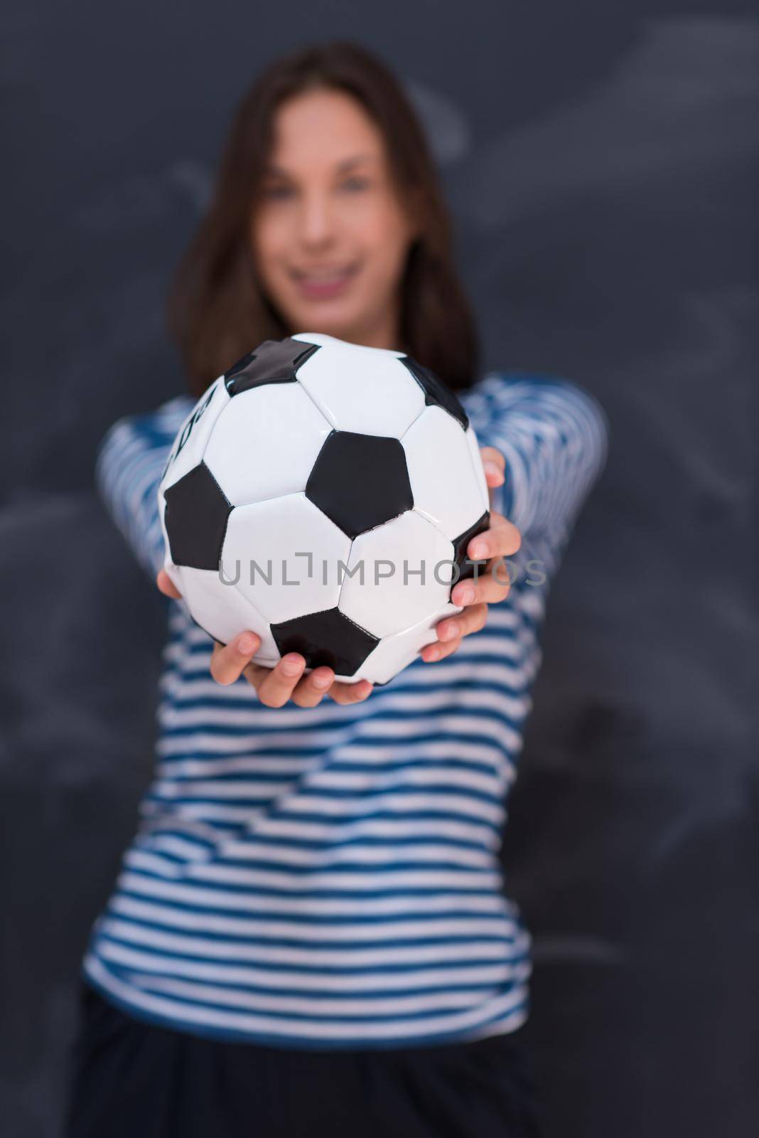 portrait of a young woman holding a soccer ball in front of chalk drawing board