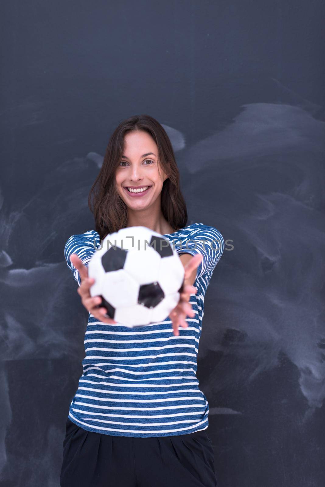 portrait of a young woman holding a soccer ball in front of chalk drawing board