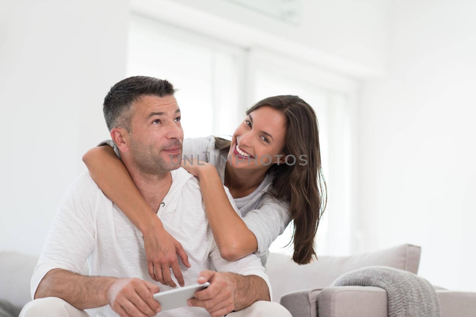 Young happy couple using mobile phone at home together, looking at screen, smiling.