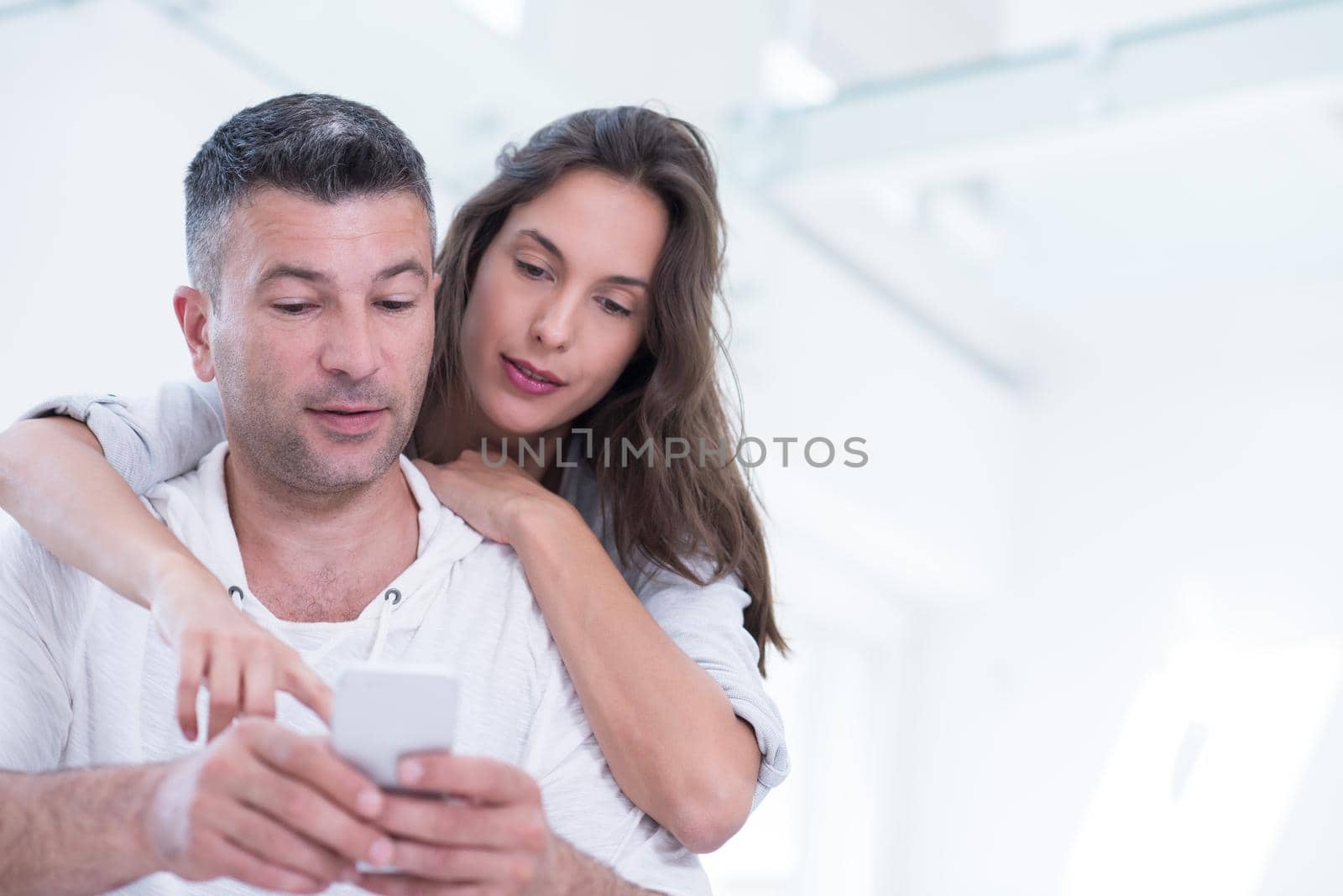 Young happy couple using mobile phone at home together, looking at screen, smiling.