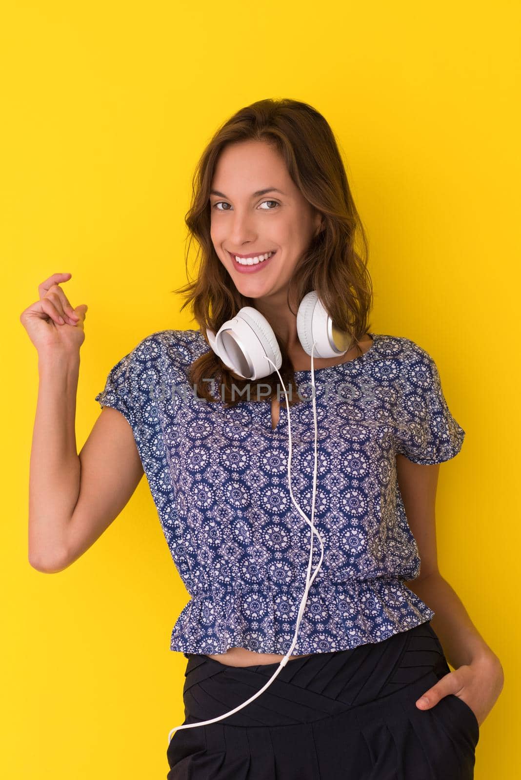 Happy young woman listening and enjoying music with headphones isolated on a yellow background