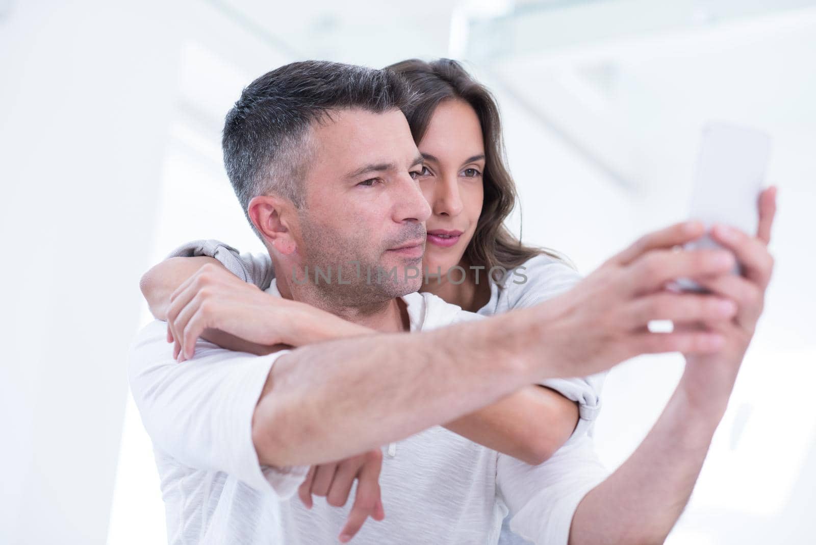 Young happy couple using mobile phone at home together, looking at screen, smiling.