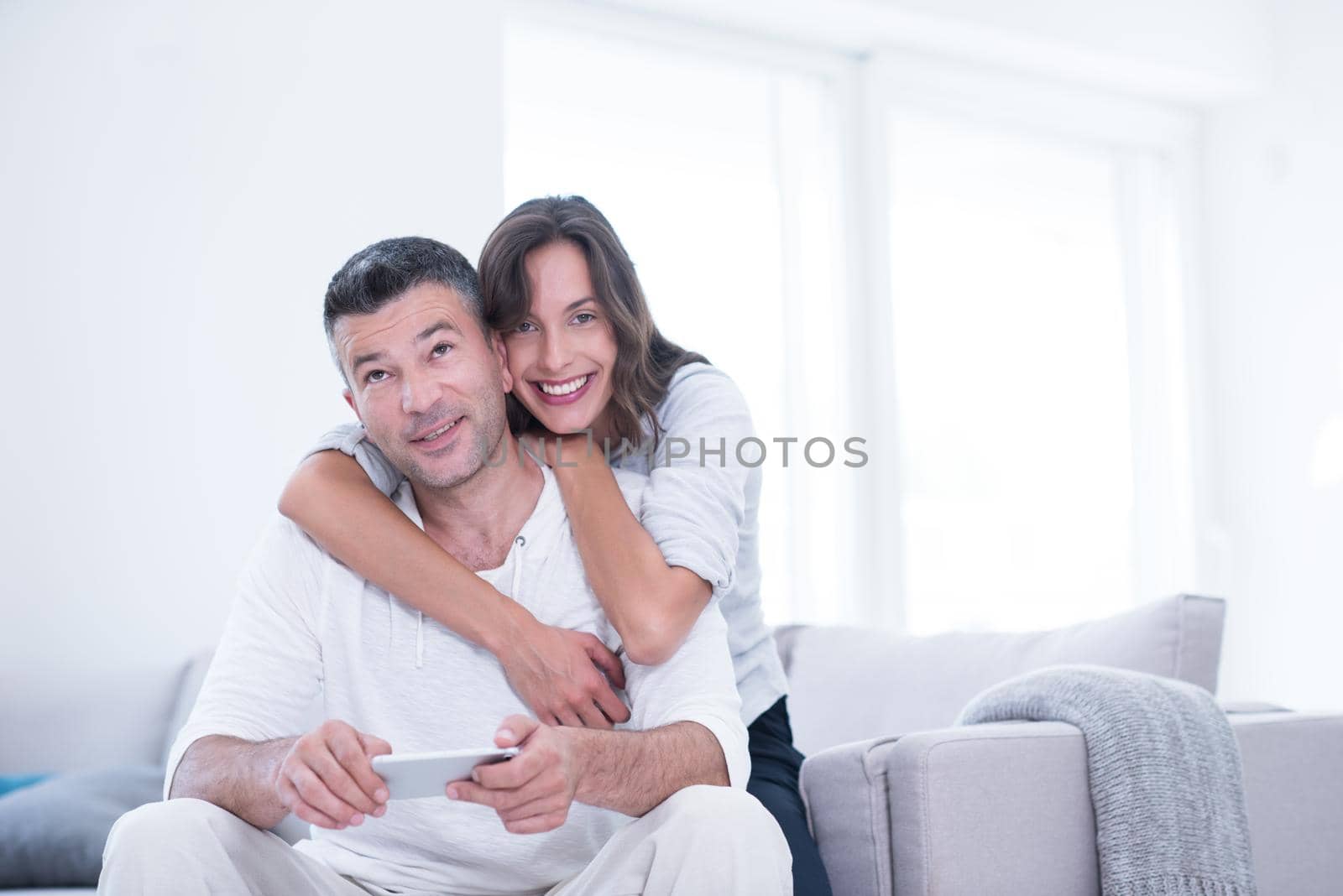 Young happy couple using mobile phone at home together, looking at screen, smiling.