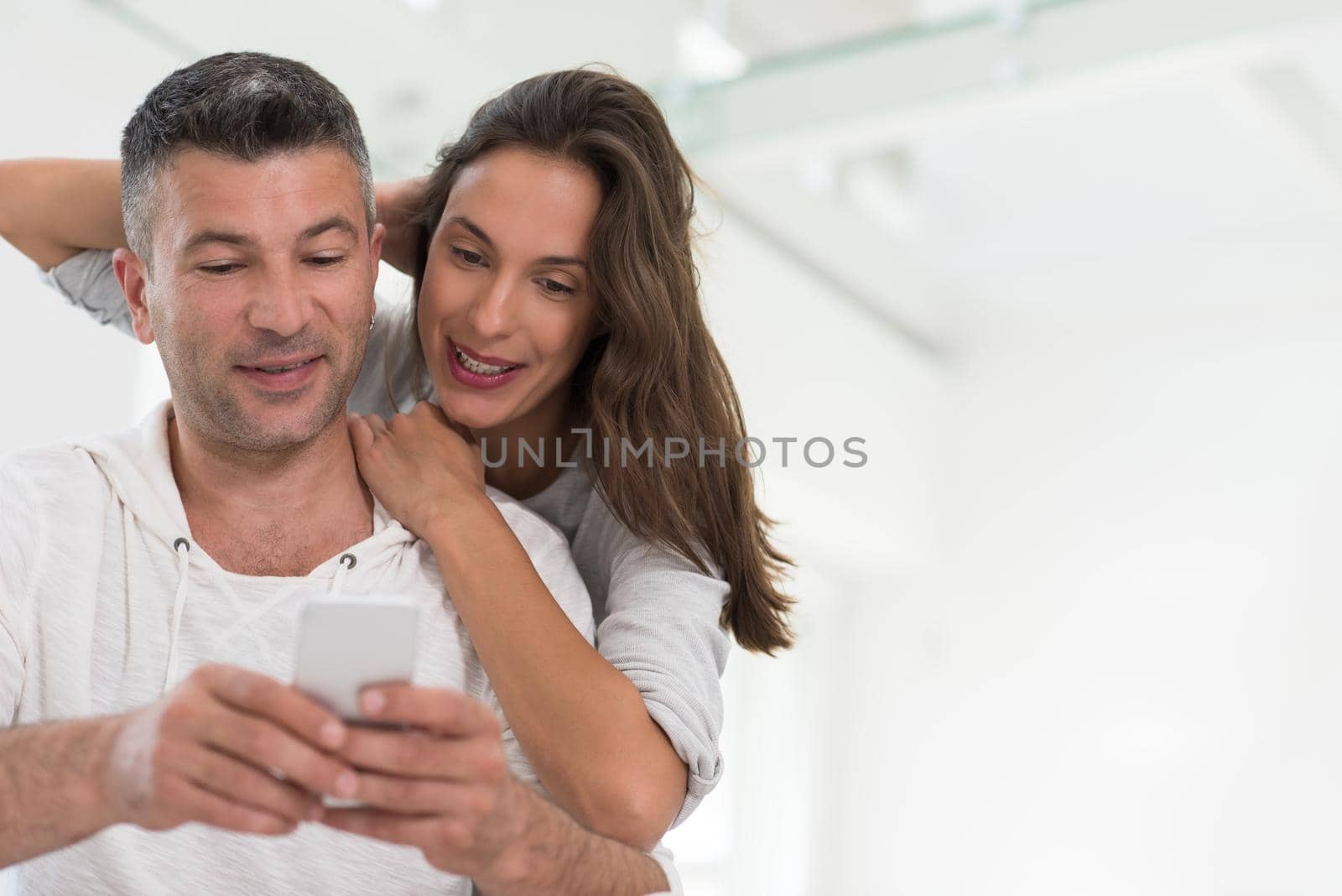 Young happy couple using mobile phone at home together, looking at screen, smiling.