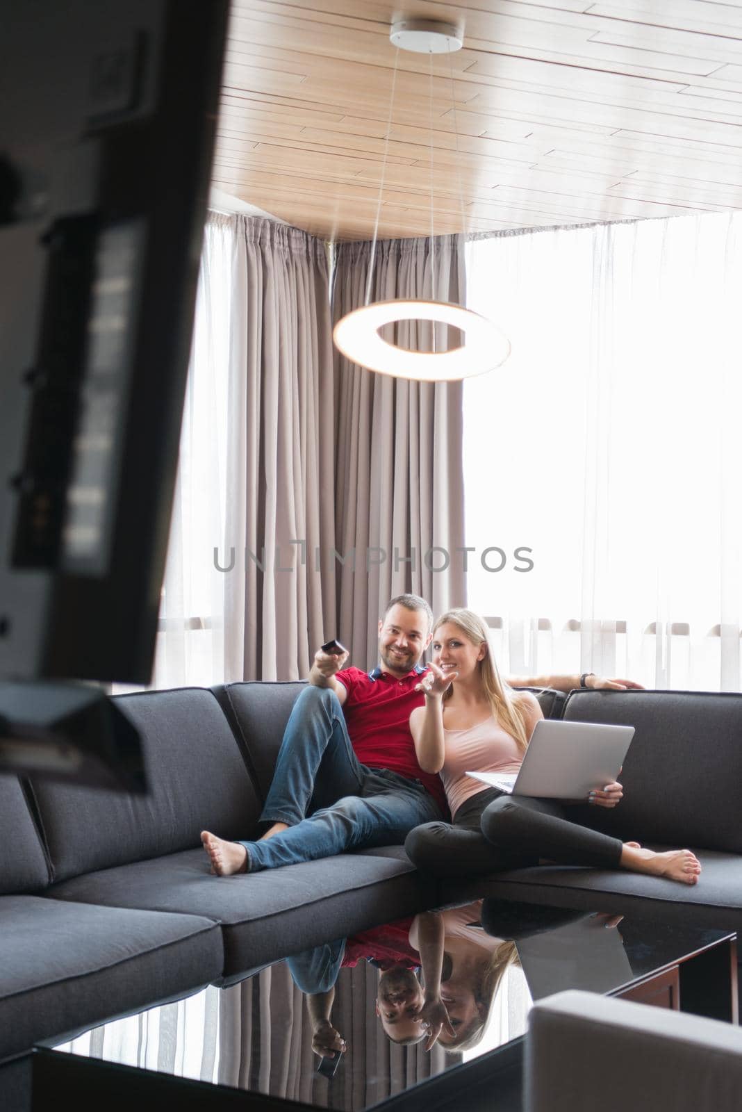 Young couple relaxes on the sofa in the luxury living room, using a laptop and remote control