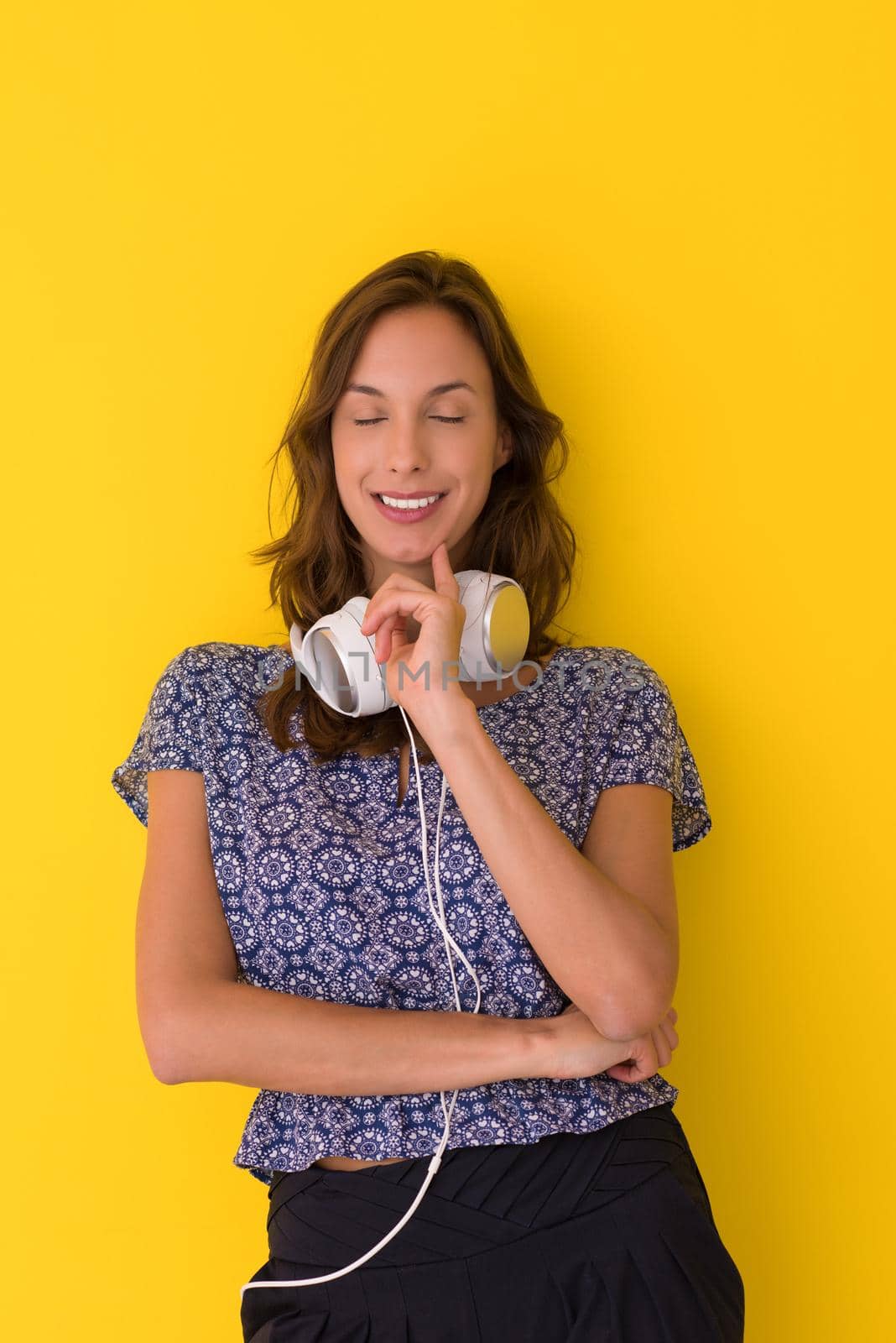 Happy young woman listening and enjoying music with headphones isolated on a yellow background