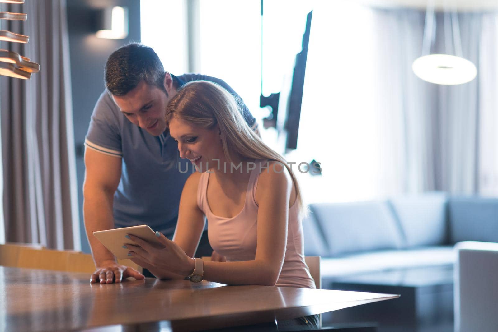 Young couple using tablet computer at luxury home together, looking at screen, smiling.