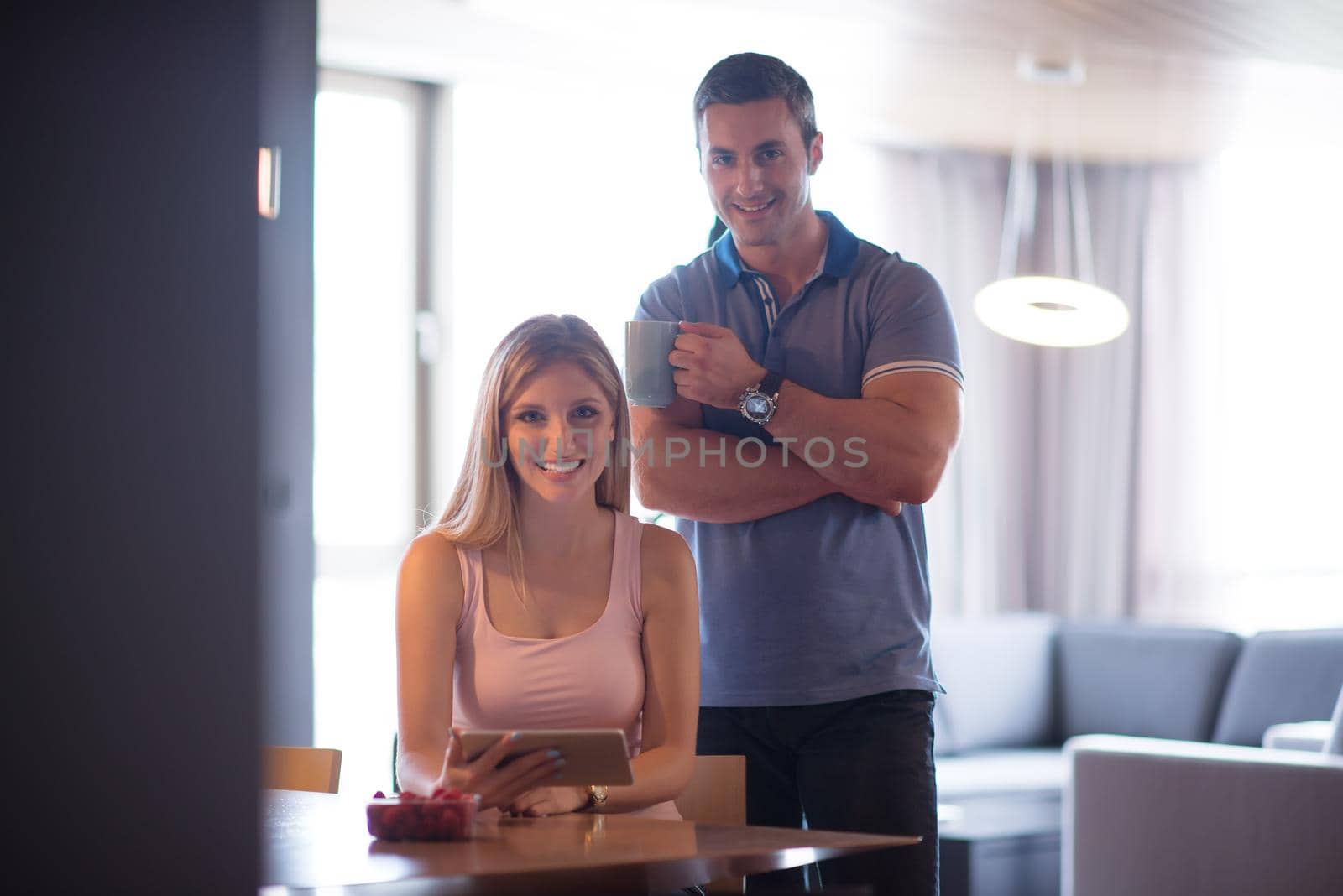 Young couple using tablet computer at luxury home together, looking at screen, smiling.