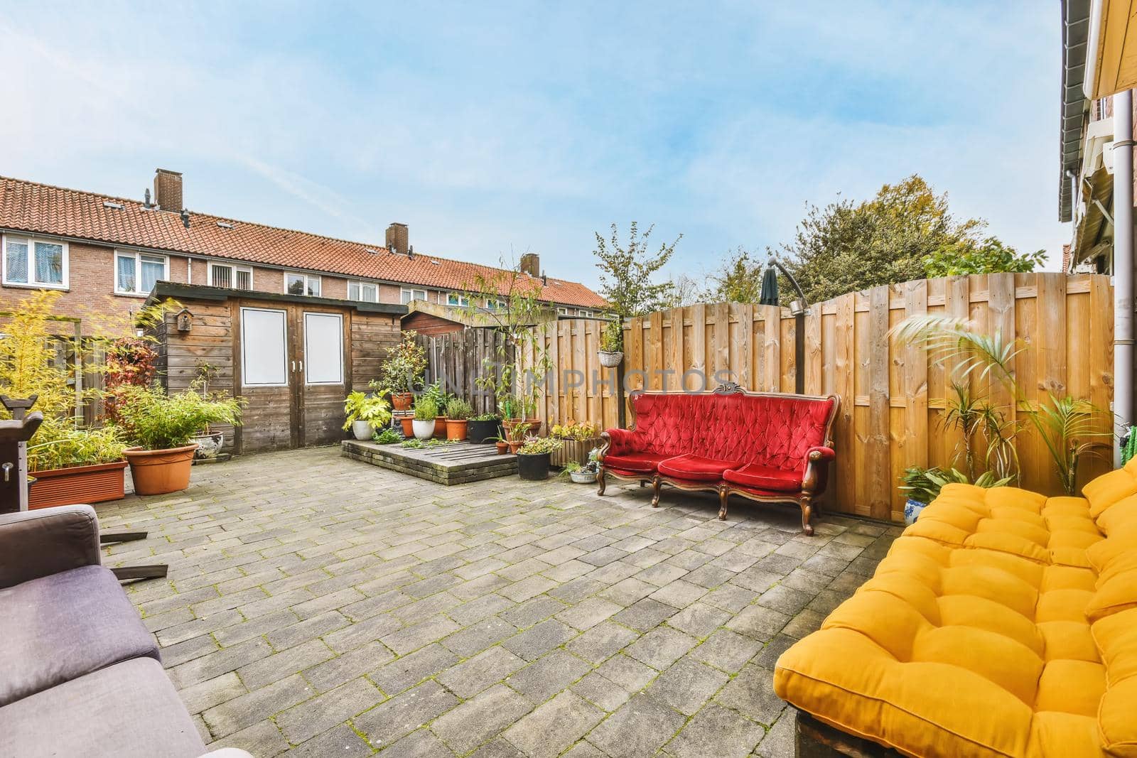 Cozy courtyard of a house with pots of flowers and a bright scarlet velvet sofa