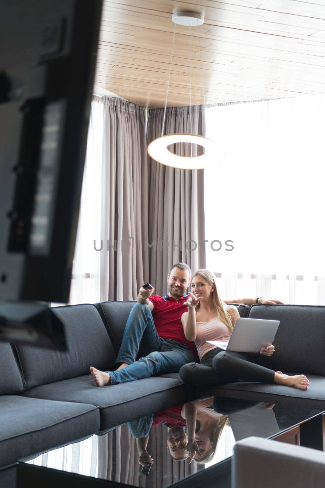 Young couple relaxes on the sofa in the luxury living room, using a laptop and remote control