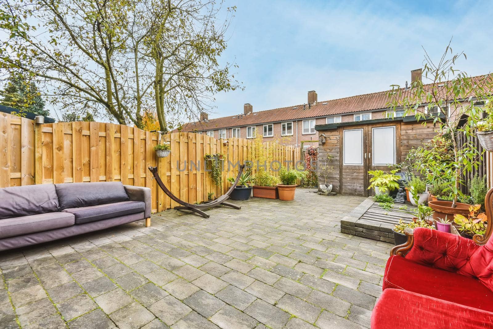 Cozy courtyard of a house with pots of flowers and a bright scarlet velvet sofa