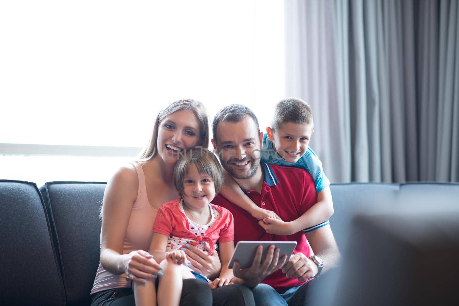 Happy Young Family Playing Together with tablet at home sitting on the sofa