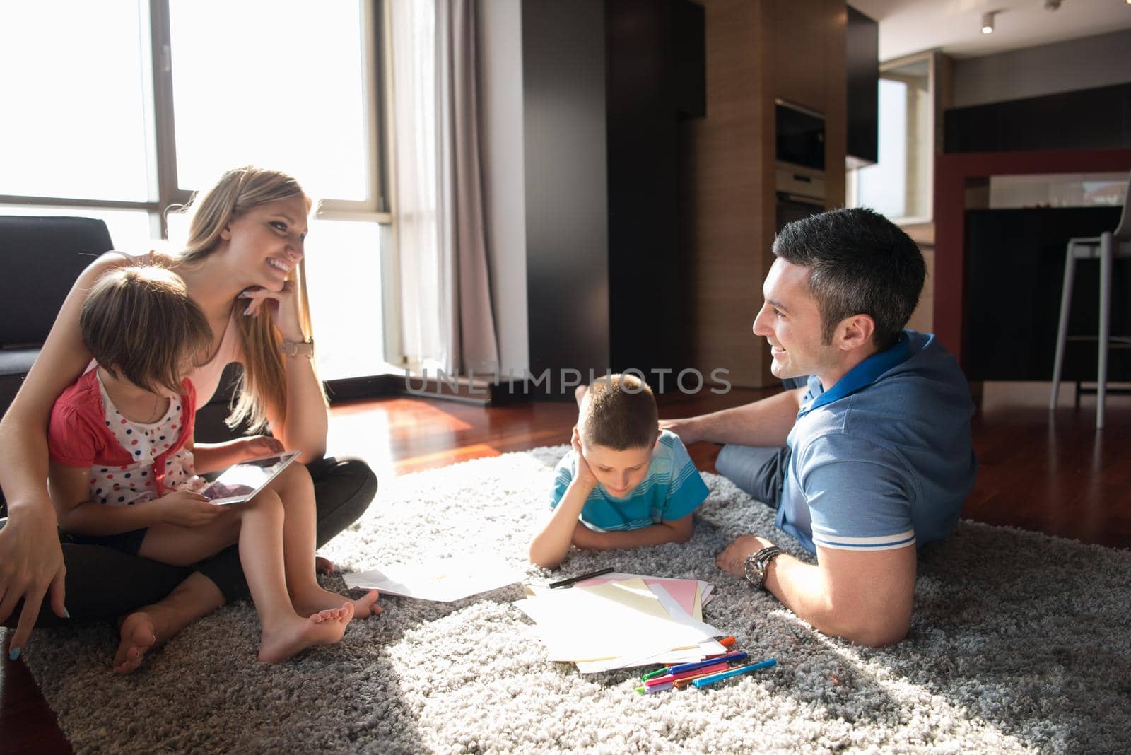 Happy Young Family Playing Together at home on the floor using a tablet and a children's drawing set