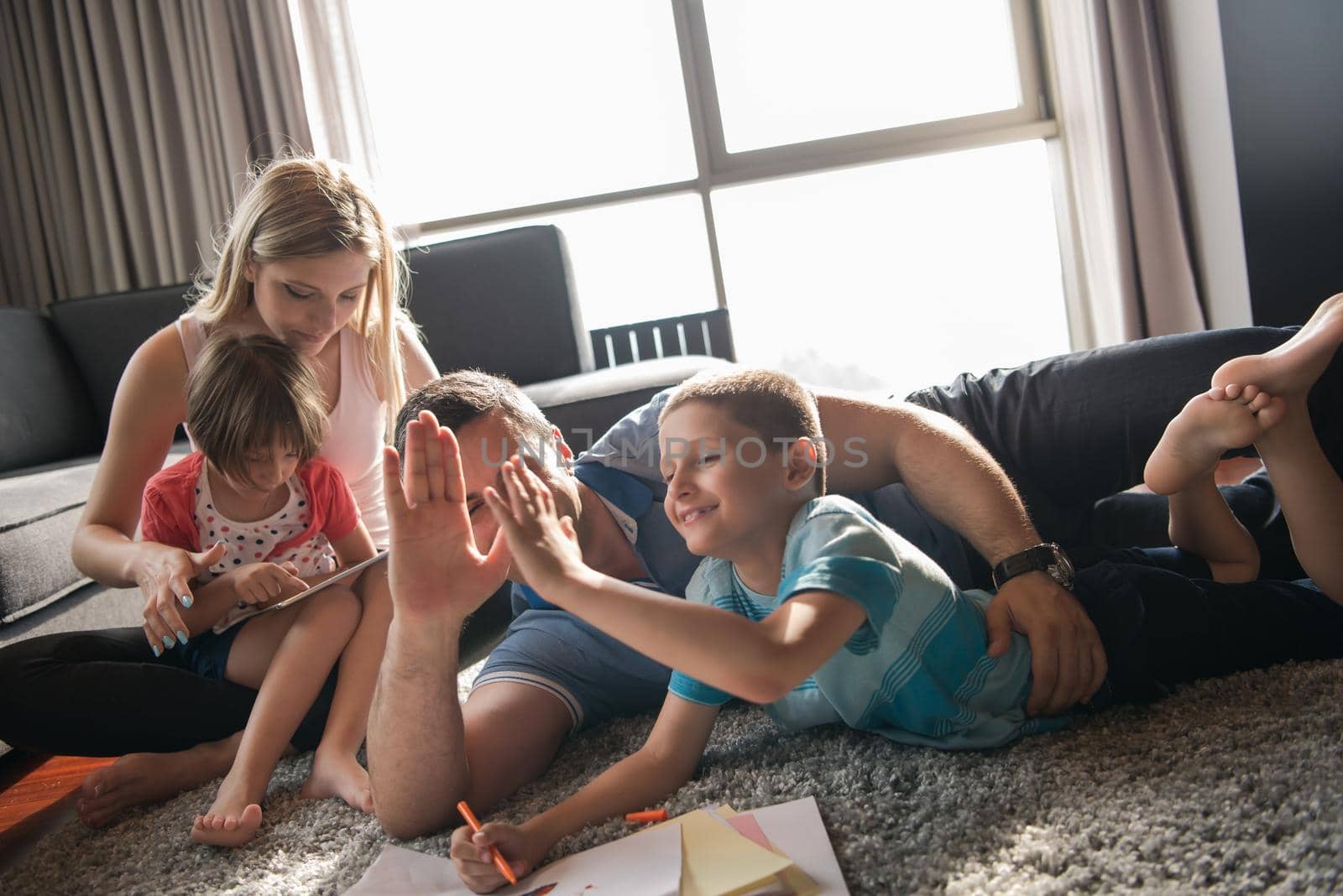 Happy Young Family Playing Together at home on the floor using a tablet and a children's drawing set