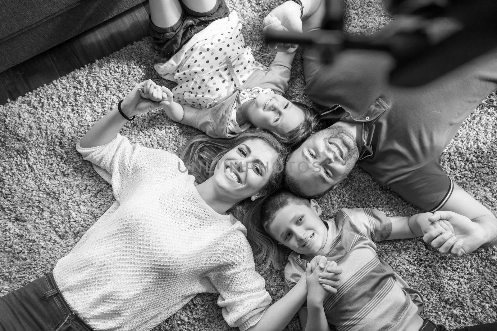 Top view of beautiful young parents, their cute little daughter and son holding hands, looking at camera and smiling, lying on the floor