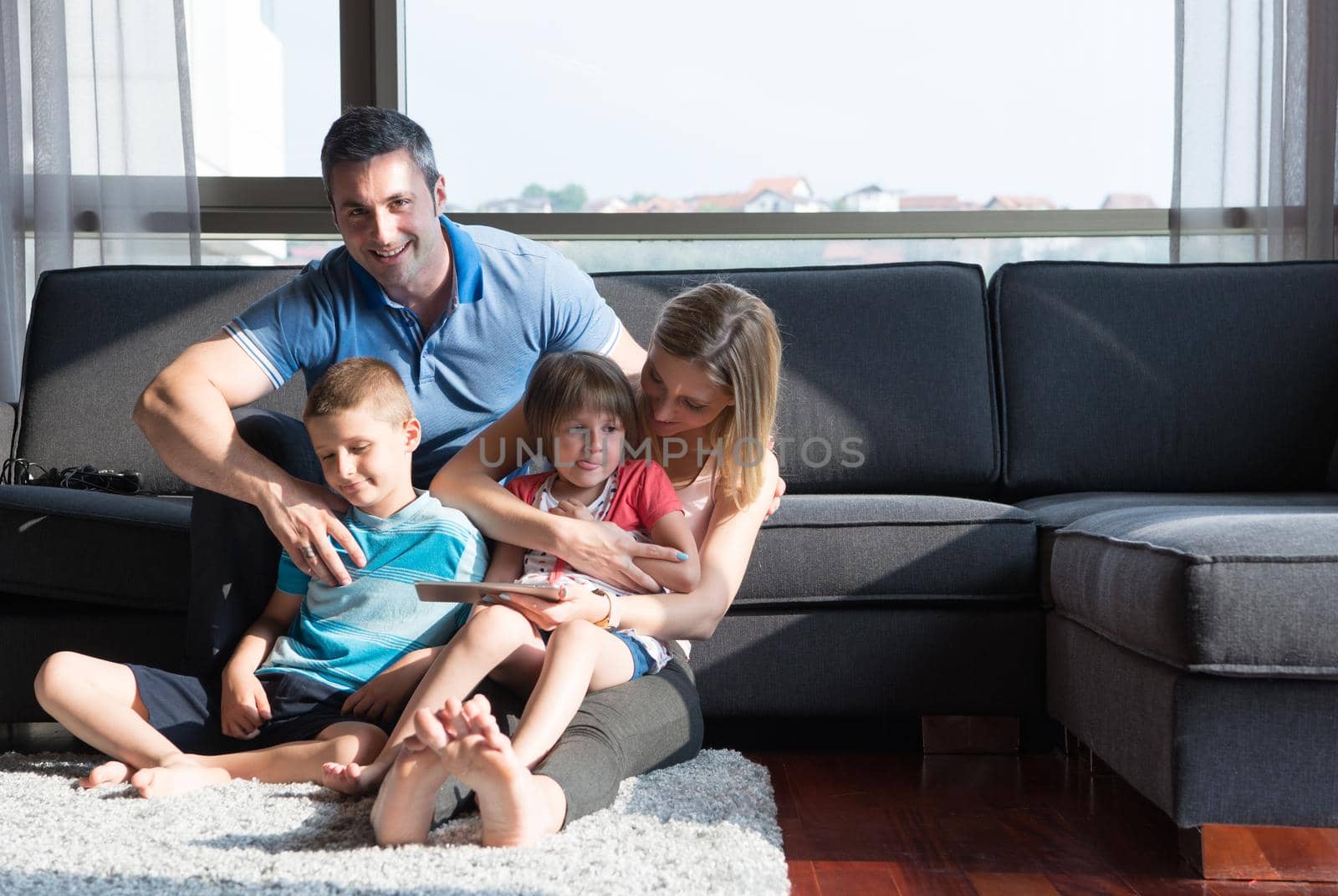 Happy Young Family Playing Together with tablet at home sitting on the sofa