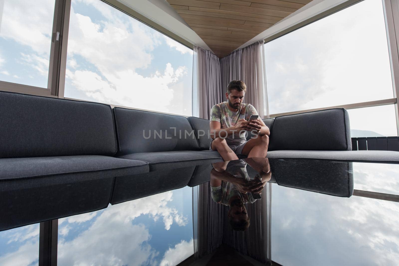 young man sitting on sofa and using a mobile phone  near the window at home