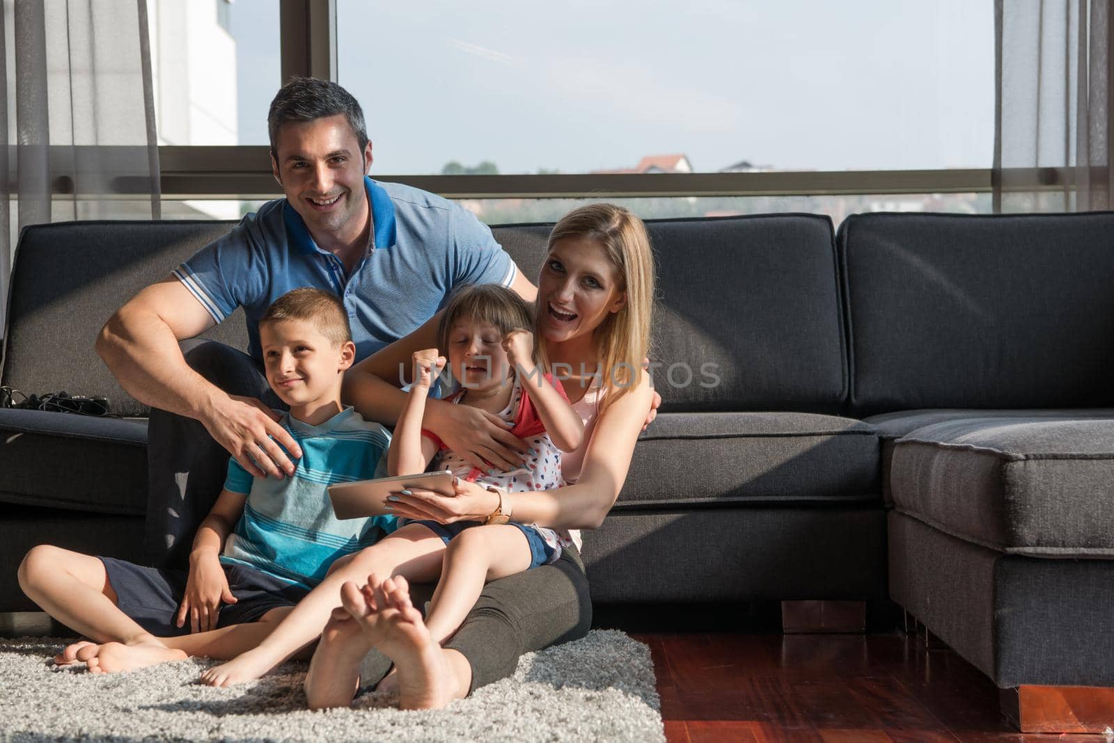 Happy Young Family Playing Together with tablet at home sitting on the sofa