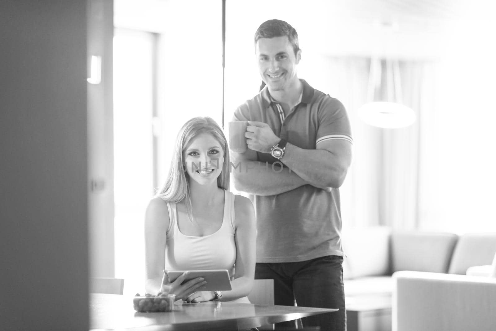 Young couple using tablet computer at luxury home together, looking at screen, smiling.