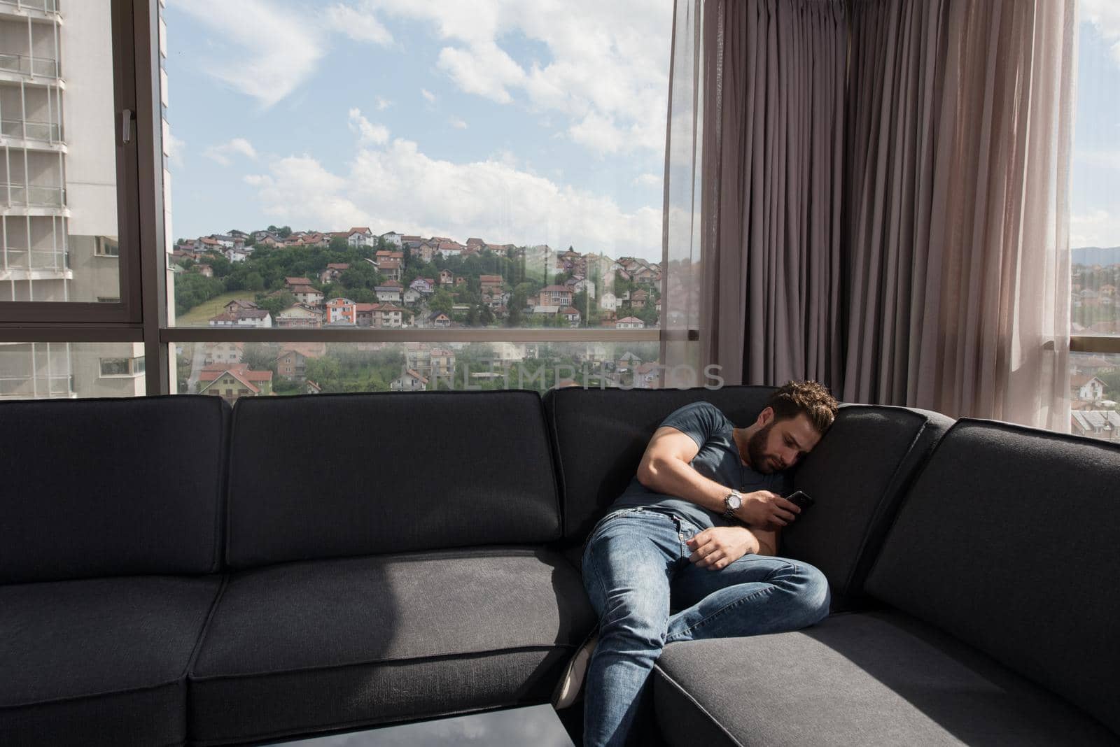 young man sitting on sofa and using a mobile phone  near the window at home