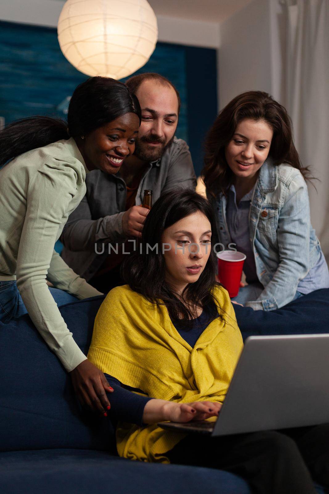 Multi-ethnic friends smiling while watching online comedy series on laptop by DCStudio