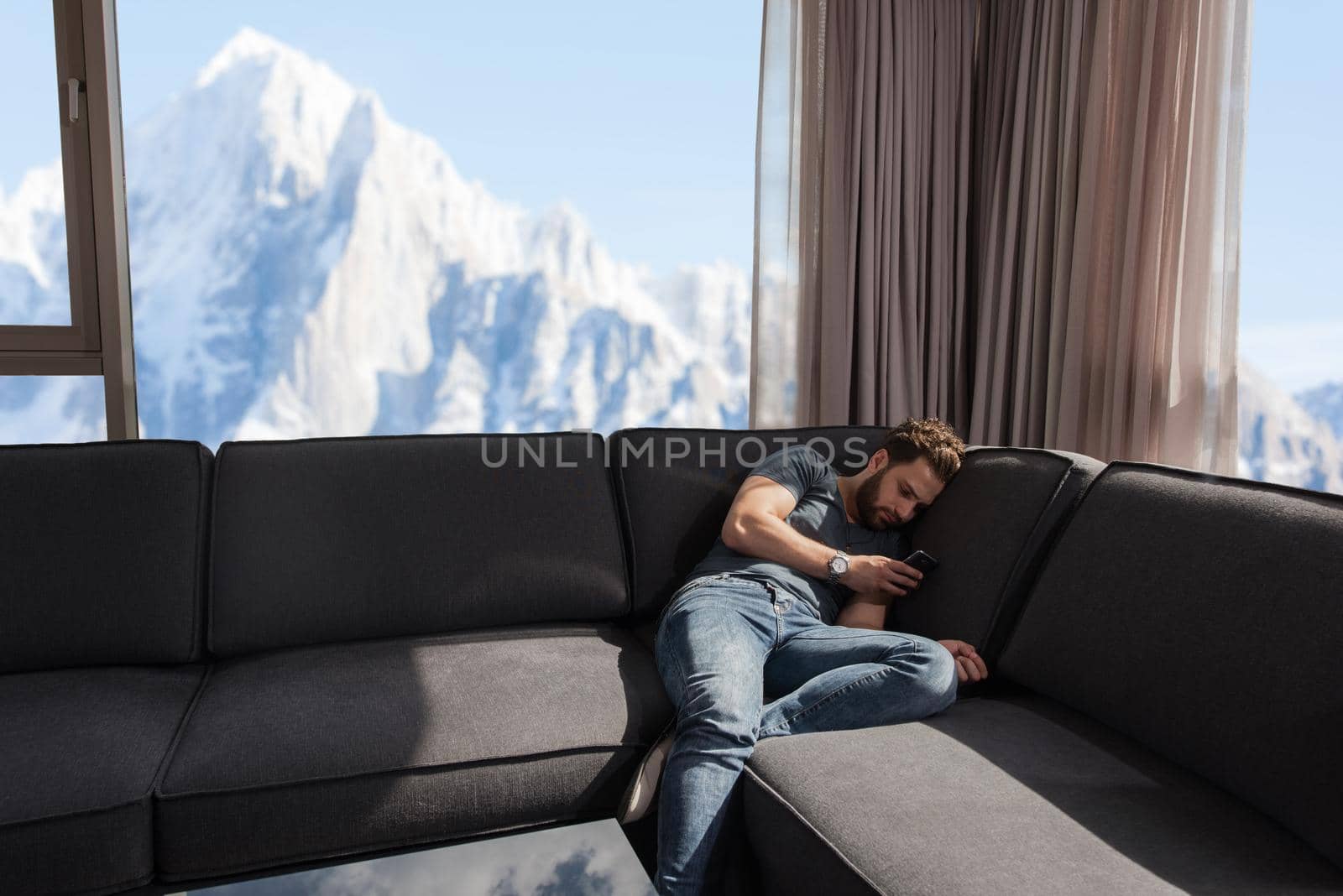 young man sitting on sofa and using a mobile phone  near the window at home