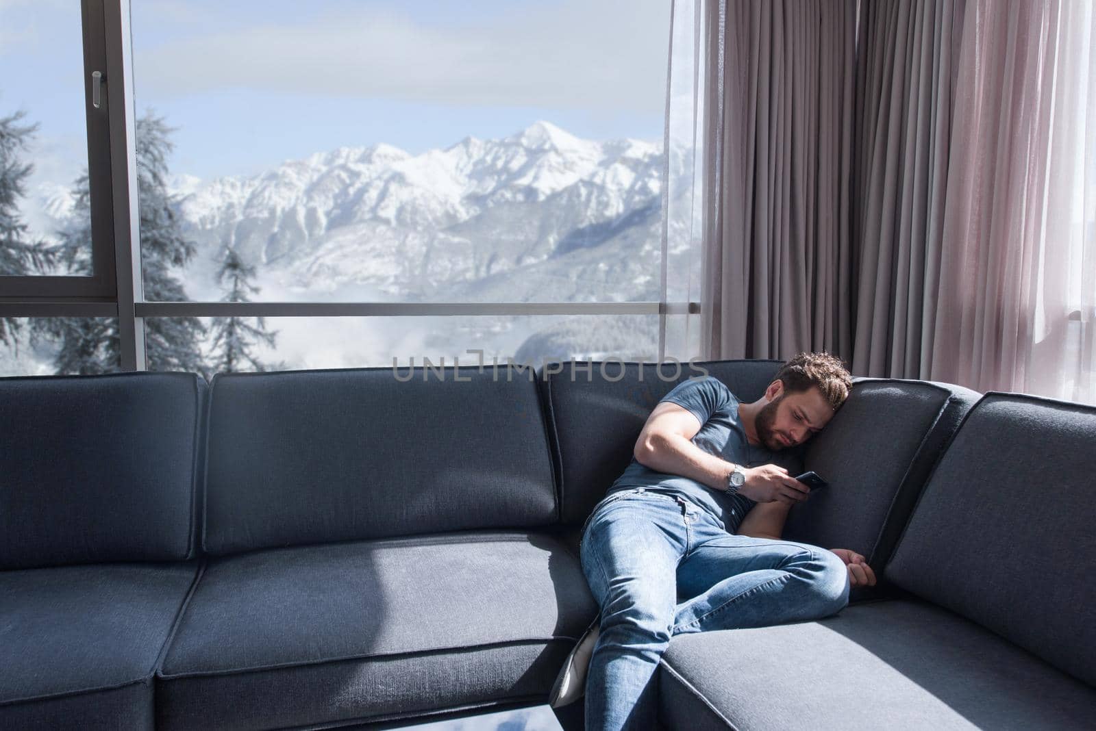 young man sitting on sofa and using a mobile phone  near the window at home