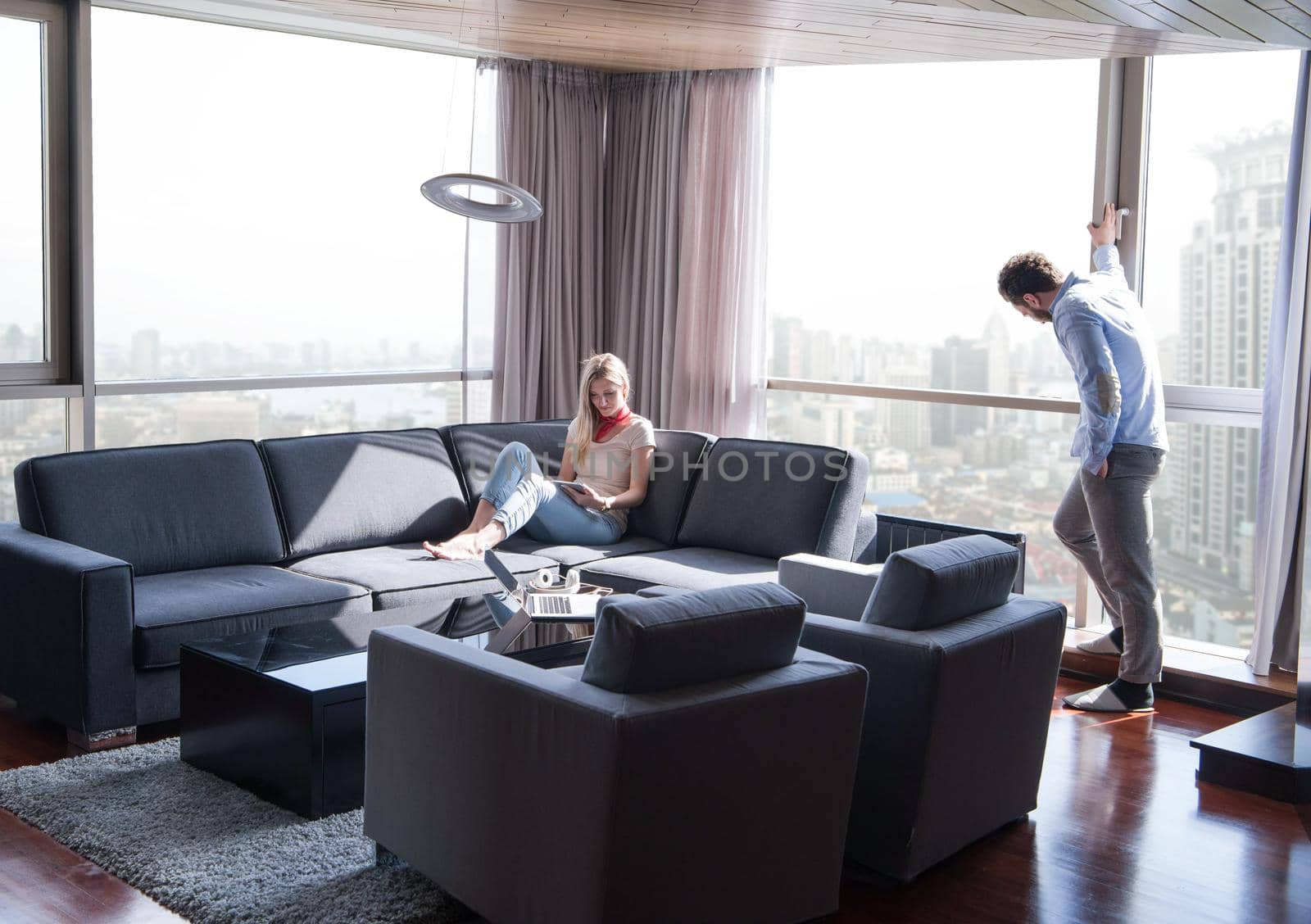 Young couple relaxing at  home using tablet computer reading in the living room near the window on the sofa couch.