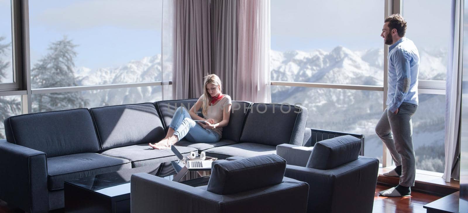 Young couple relaxing at  home using tablet computer reading in the living room near the window on the sofa couch.