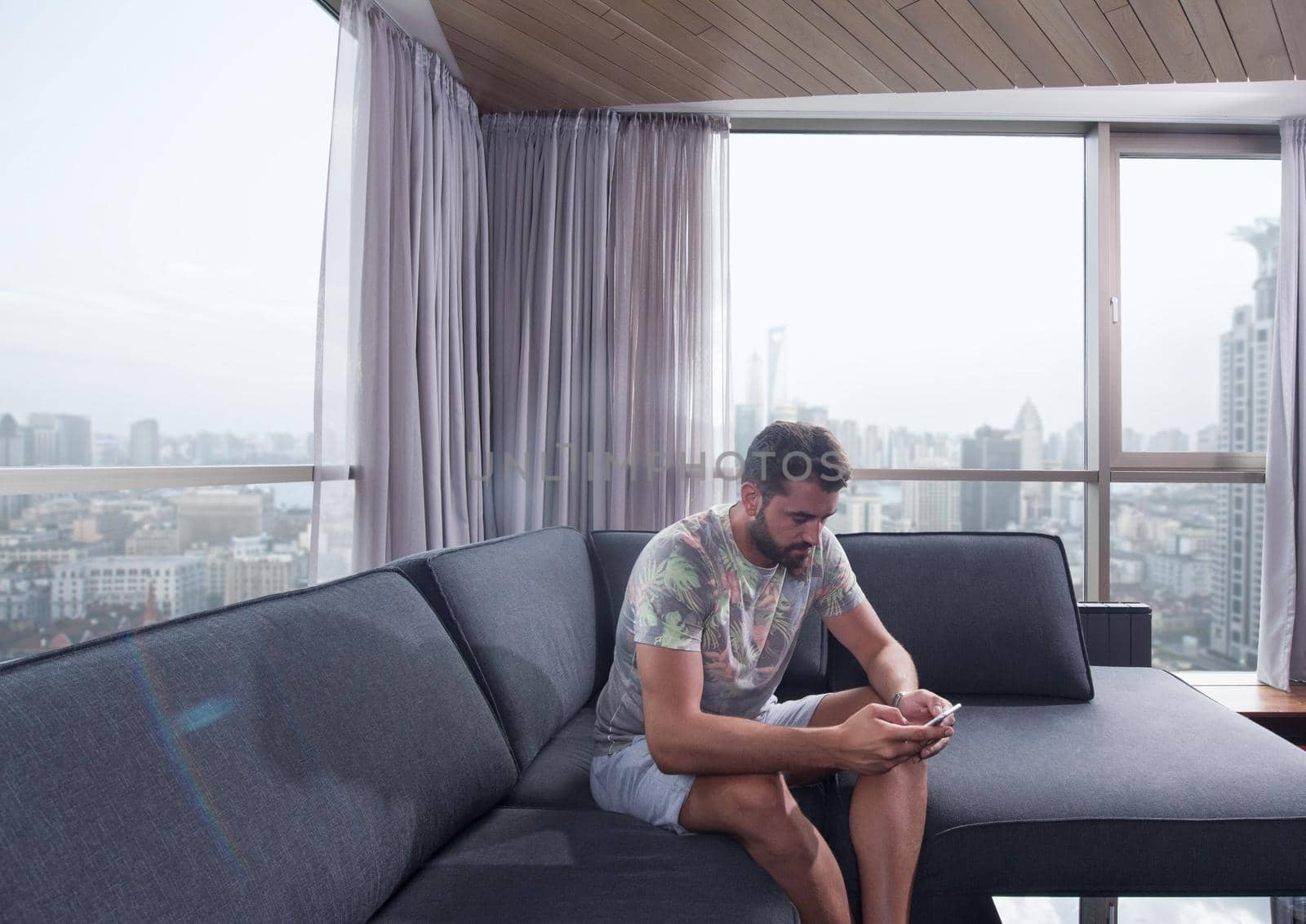 young man sitting on sofa and using a mobile phone  near the window at home