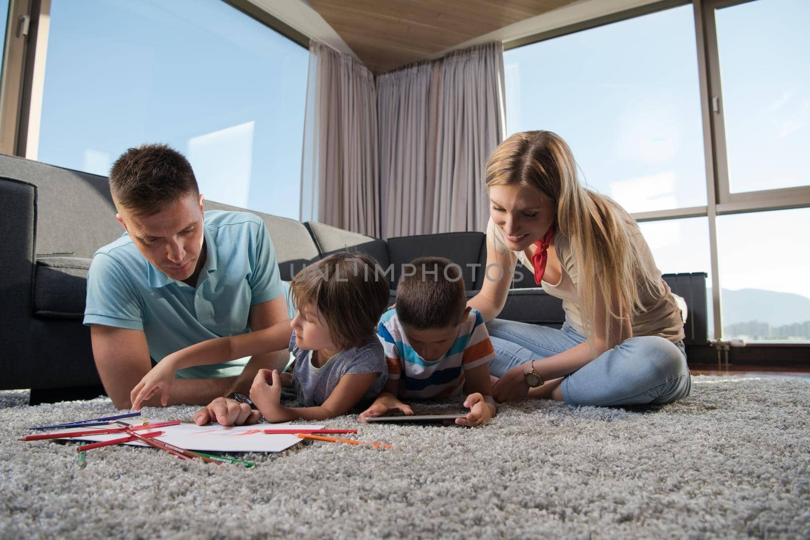 Happy Young Family Playing Together at home on the floor using a tablet and a children's drawing set