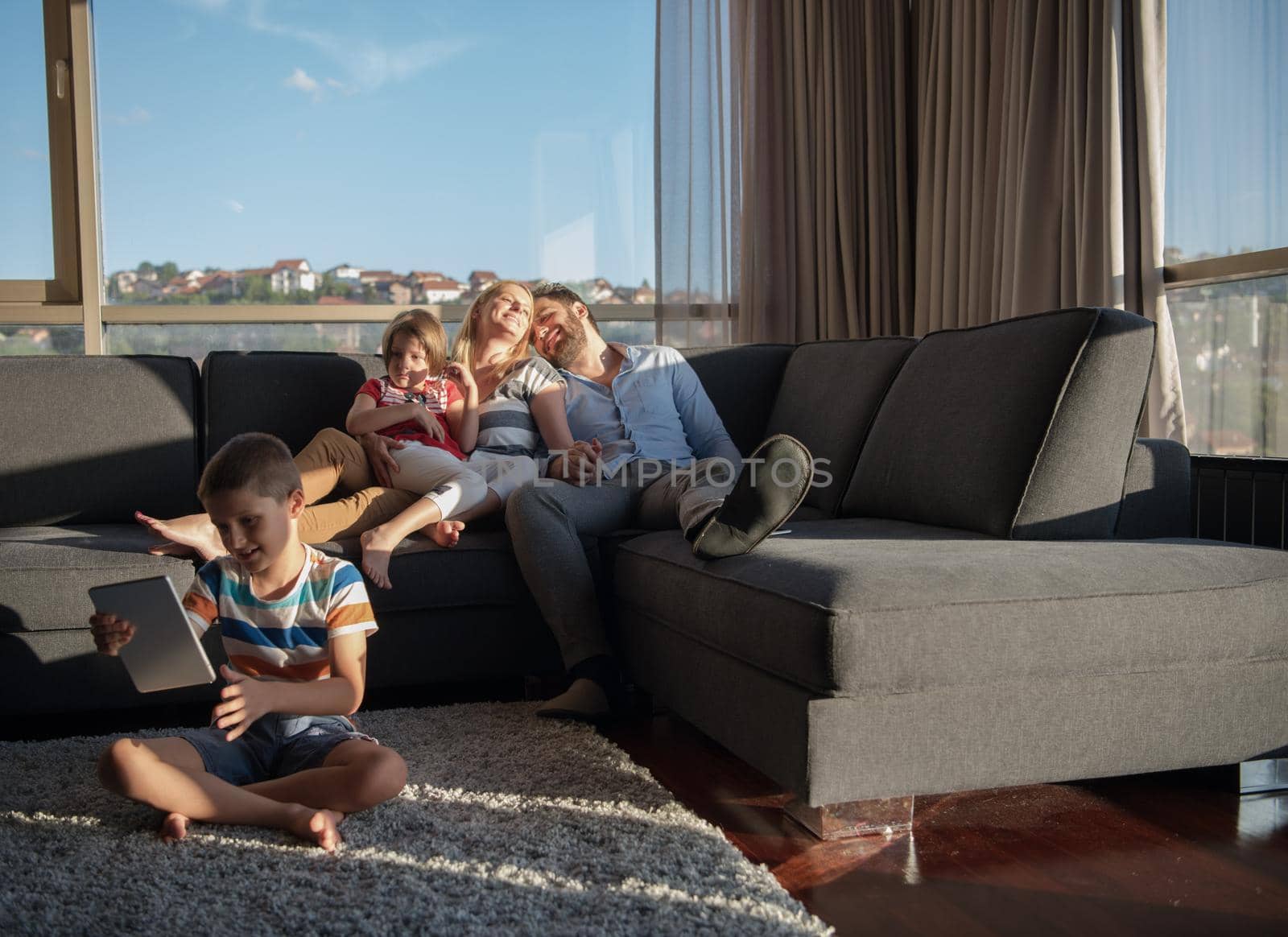 happy couple spending time with kids using tablet computer on sofa at home