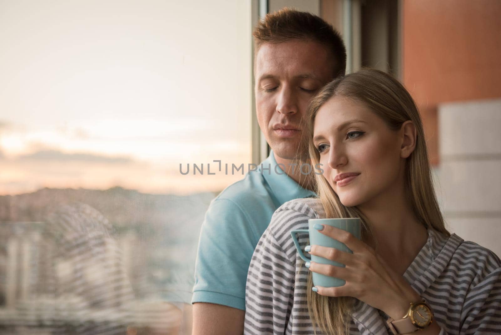 romantic happy young couple enjoying evening coffee and beautiful sunset landscape of the city while standing by the window