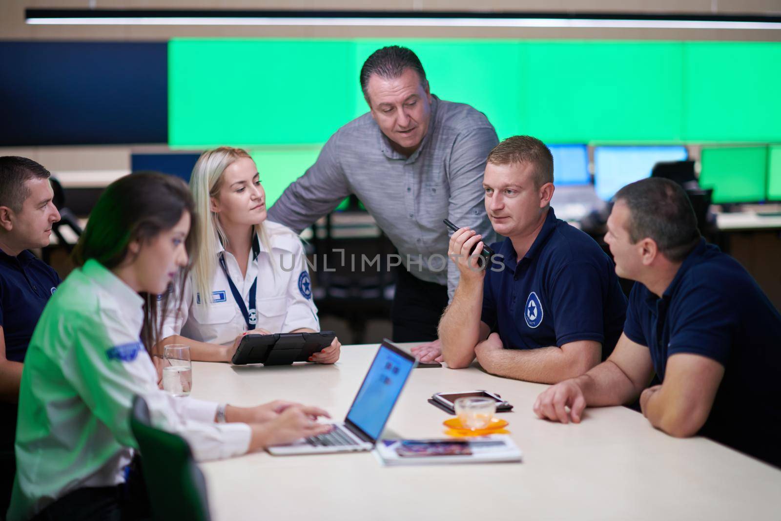 Group of security guards sitting and having briefing In the system control room  They're working in security data center surrounded by multiple Screens