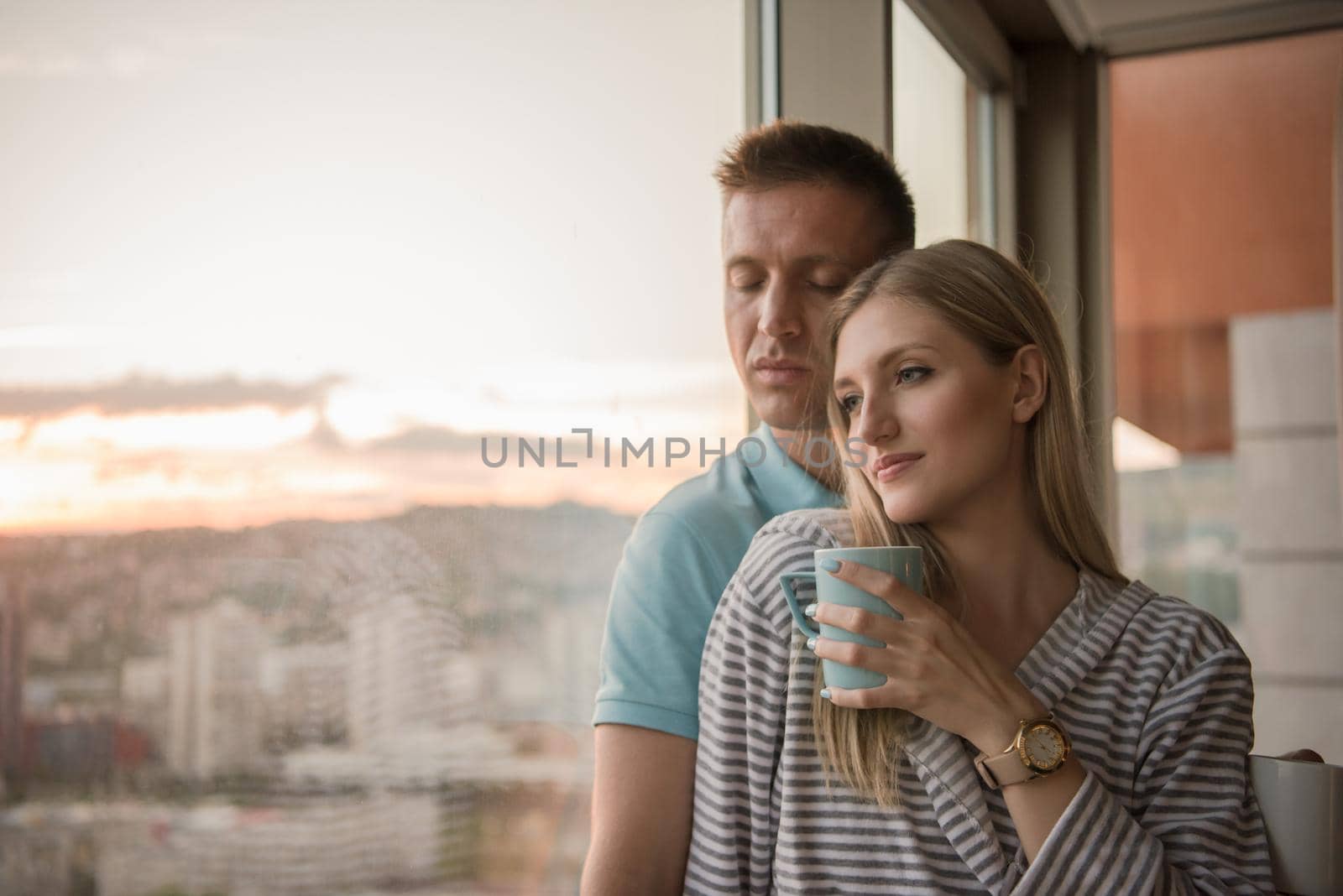 romantic happy young couple enjoying evening coffee and beautiful sunset landscape of the city while standing by the window