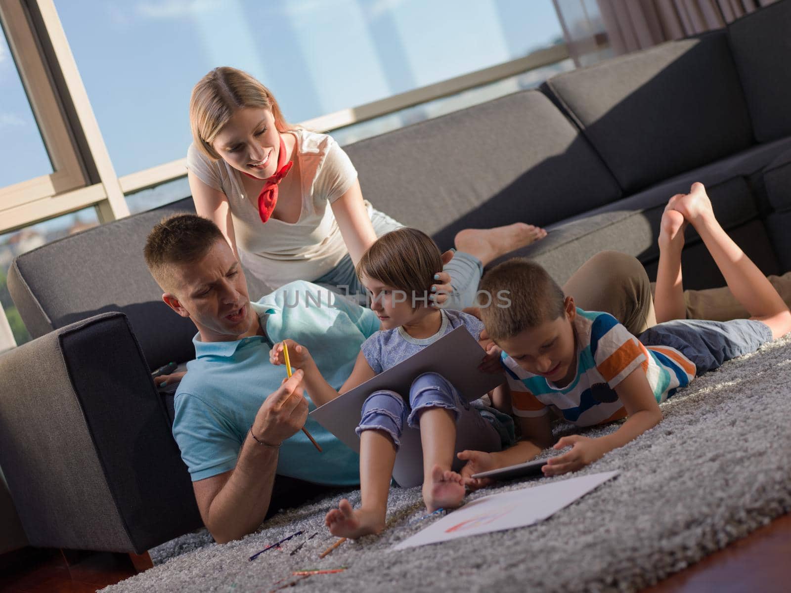 Happy Young Family Playing Together at home using a tablet and a children's drawing set