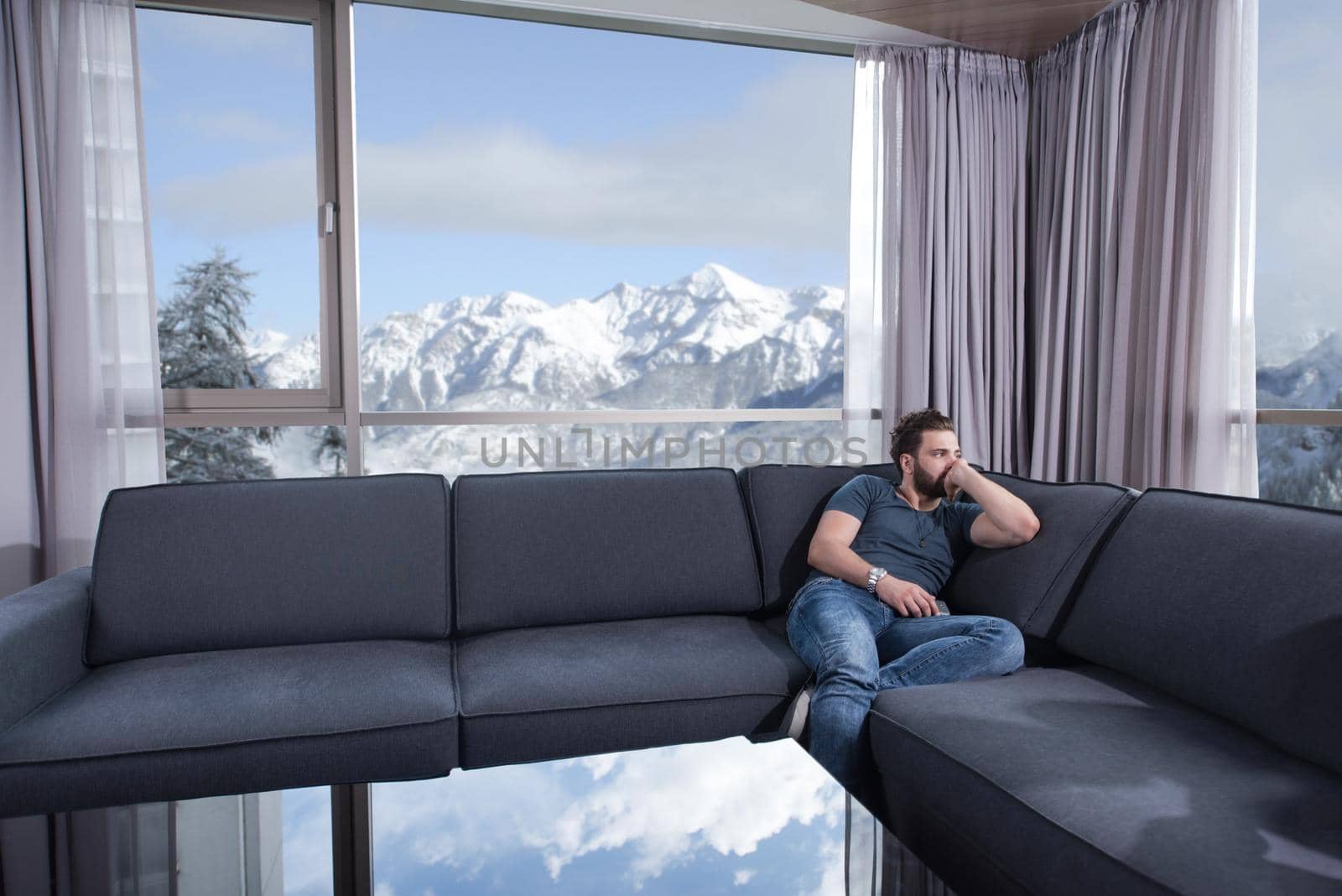 young man sitting on sofa and using a mobile phone  near the window at home