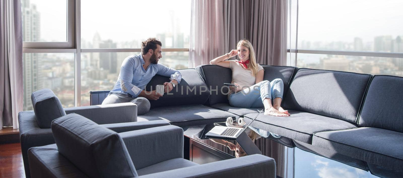 Young couple relaxing at  home using tablet computer reading in the living room near the window on the sofa couch.