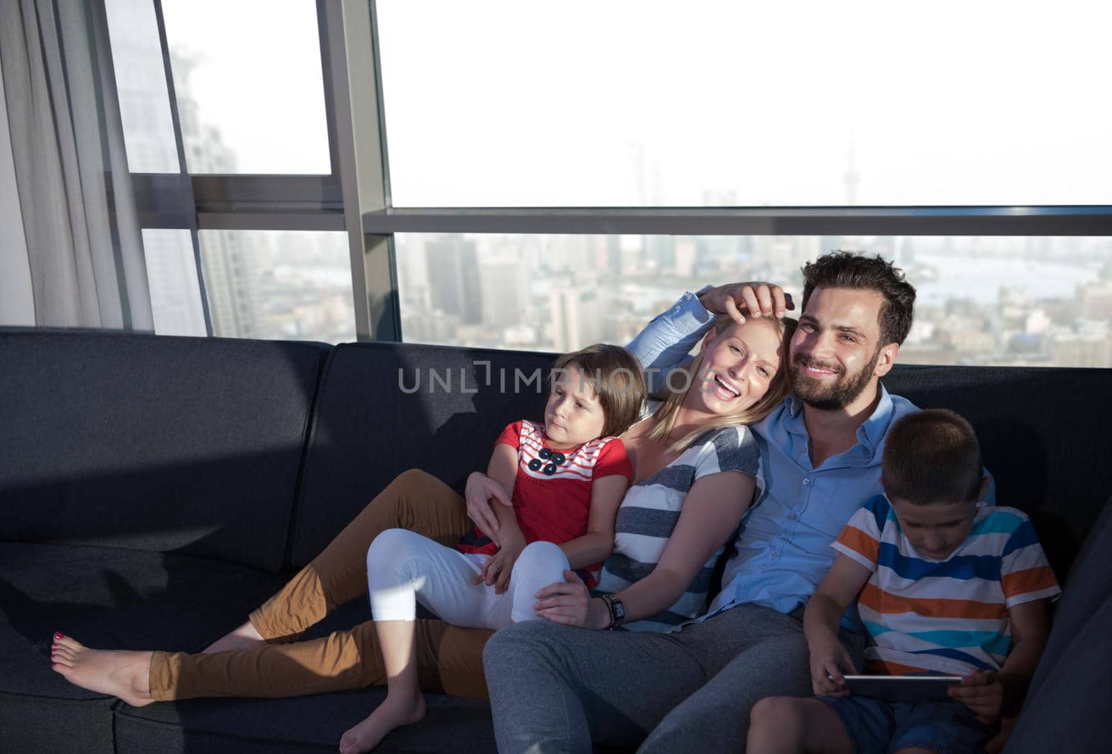 happy couple spending time with kids using tablet computer on sofa at home