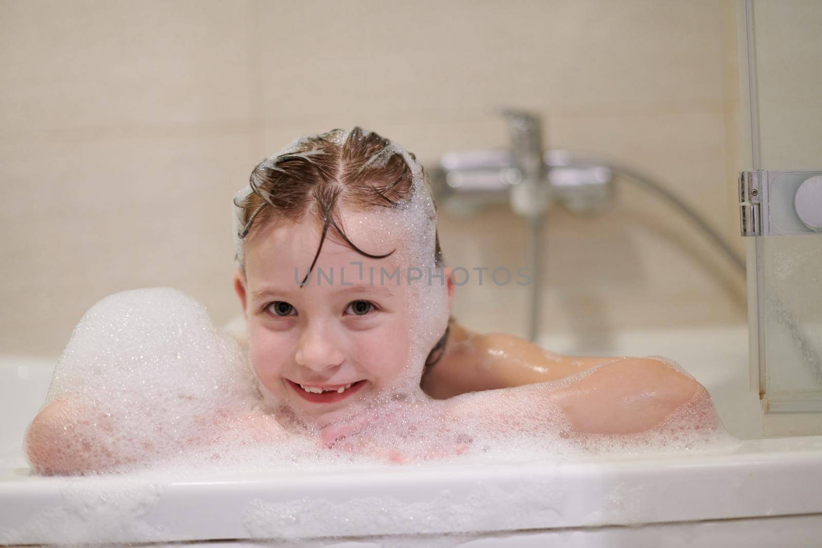 little girl playing with soap foam in bath during coronavirus stay at home pandemic quarantine