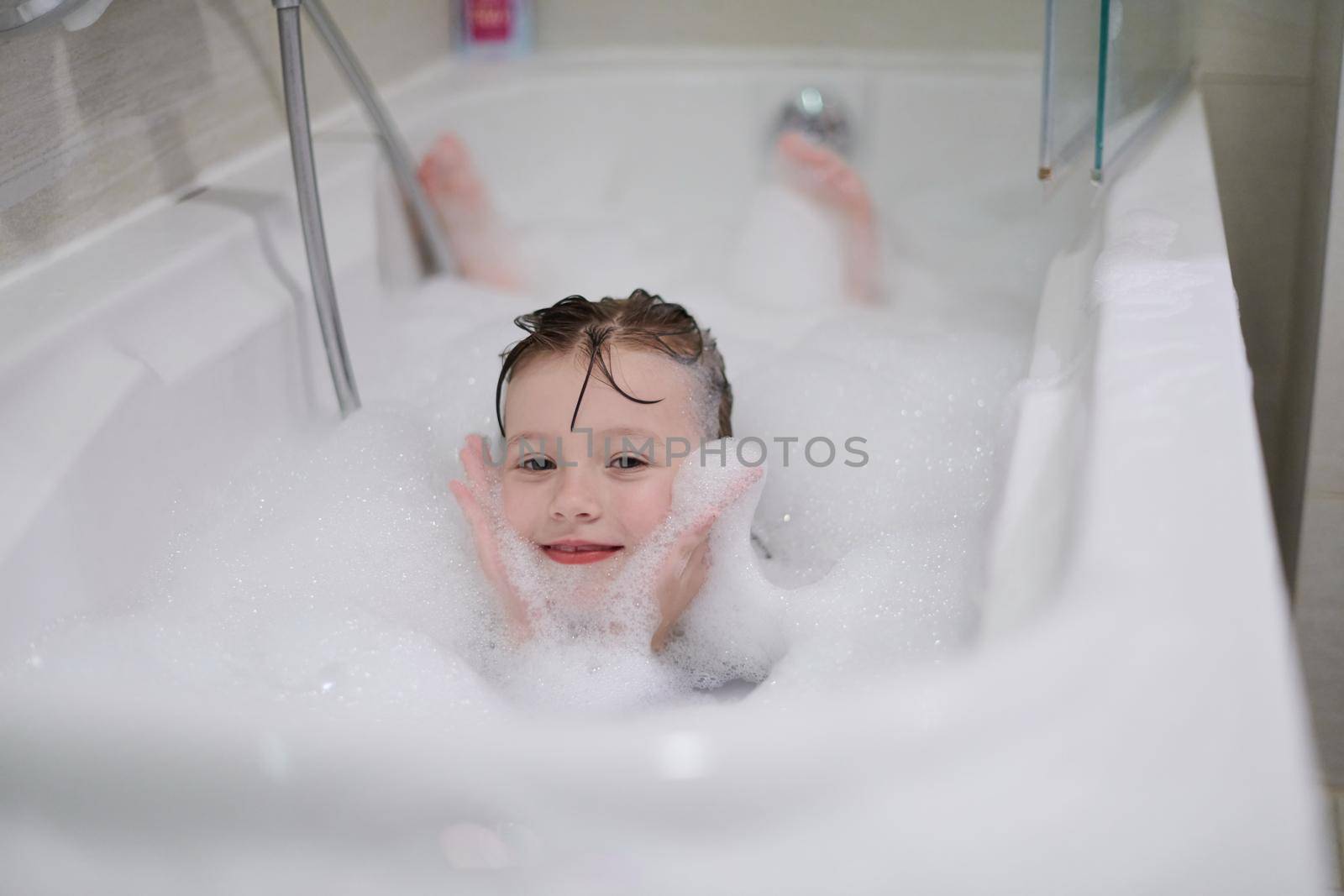 little girl playing with soap foam in bath during coronavirus stay at home pandemic quarantine