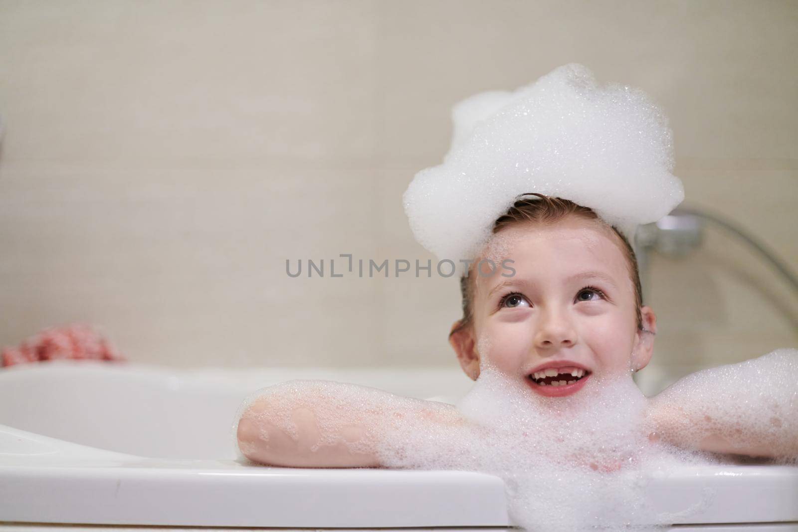 little girl playing with soap foam in bath during coronavirus stay at home pandemic quarantine