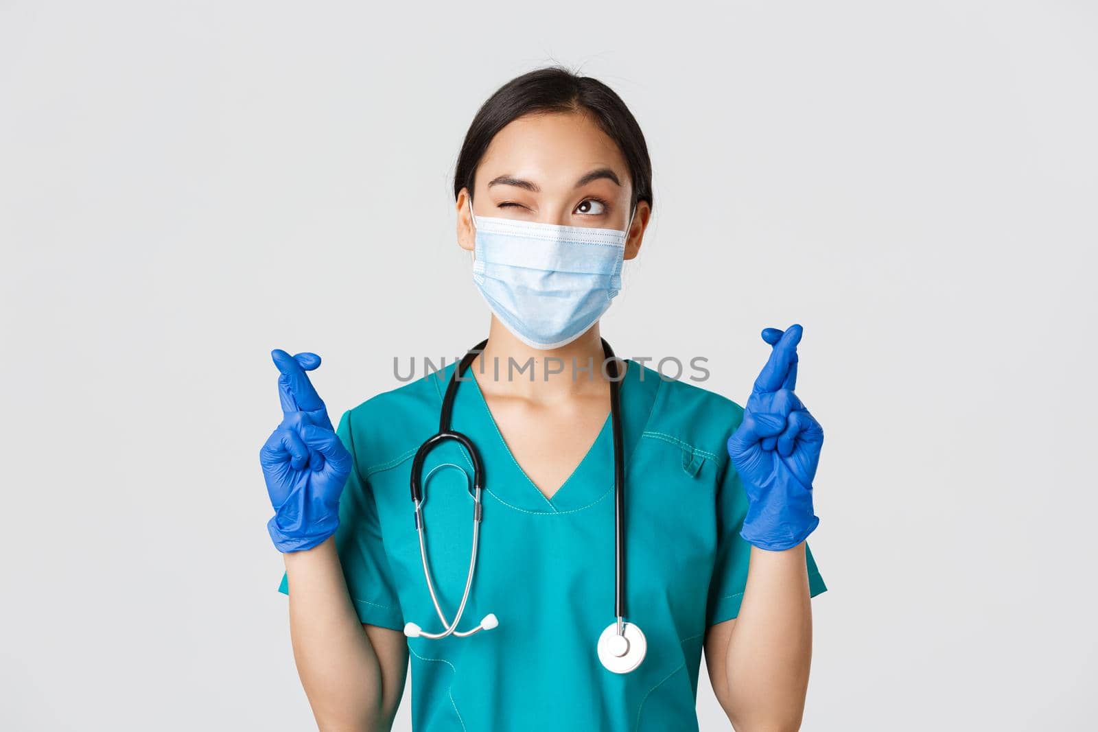 Covid-19, coronavirus disease, healthcare workers concept. Hopeful asian female physician in medical mask and gloves, looking upper left corner and praying, making wish, white background by Benzoix