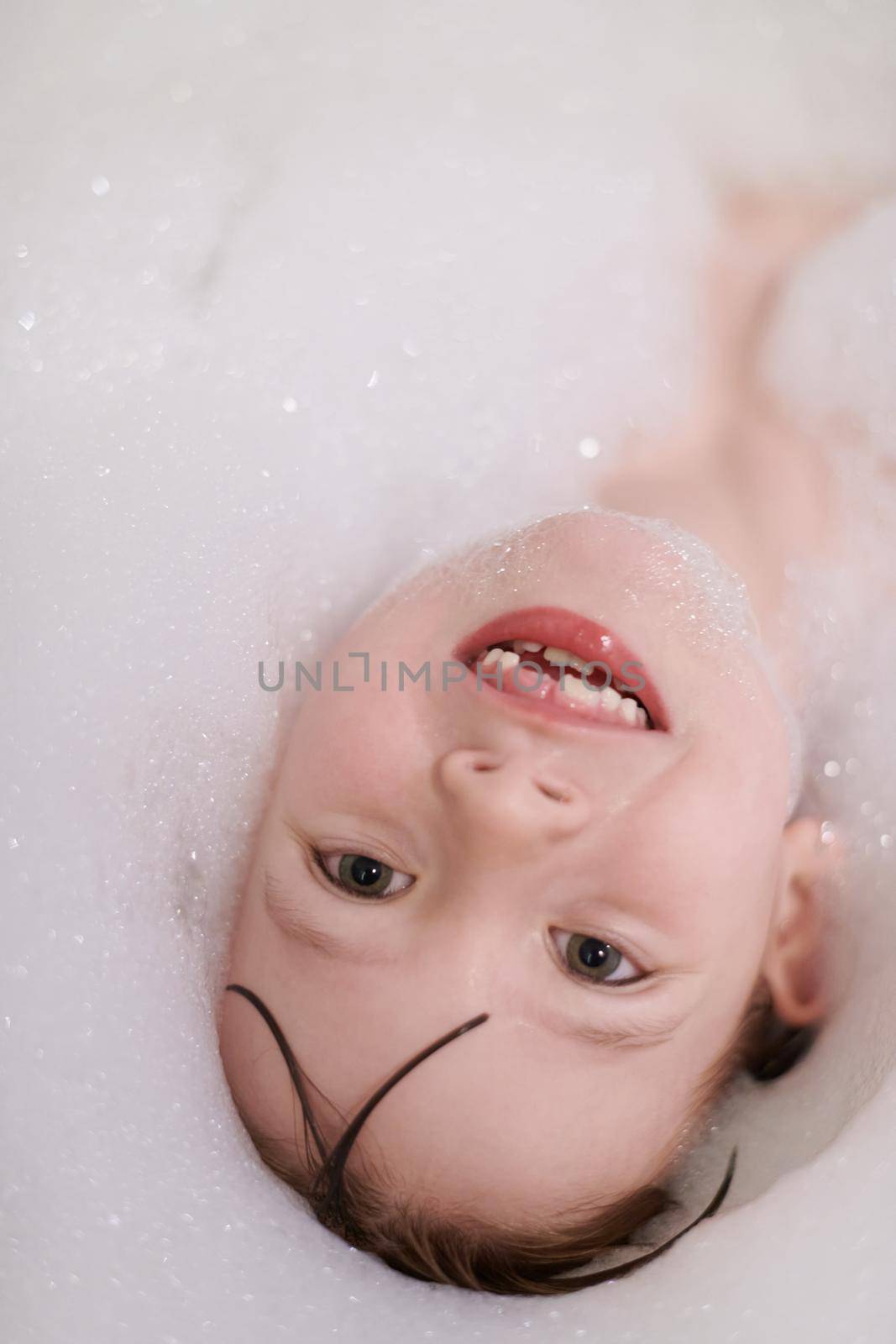 little girl playing with soap foam in bath during coronavirus stay at home pandemic quarantine